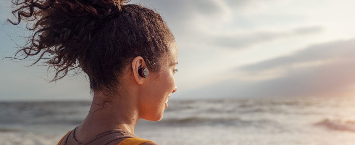 Nainen rannalla täysin langattomat kuulokkeet korvissaan